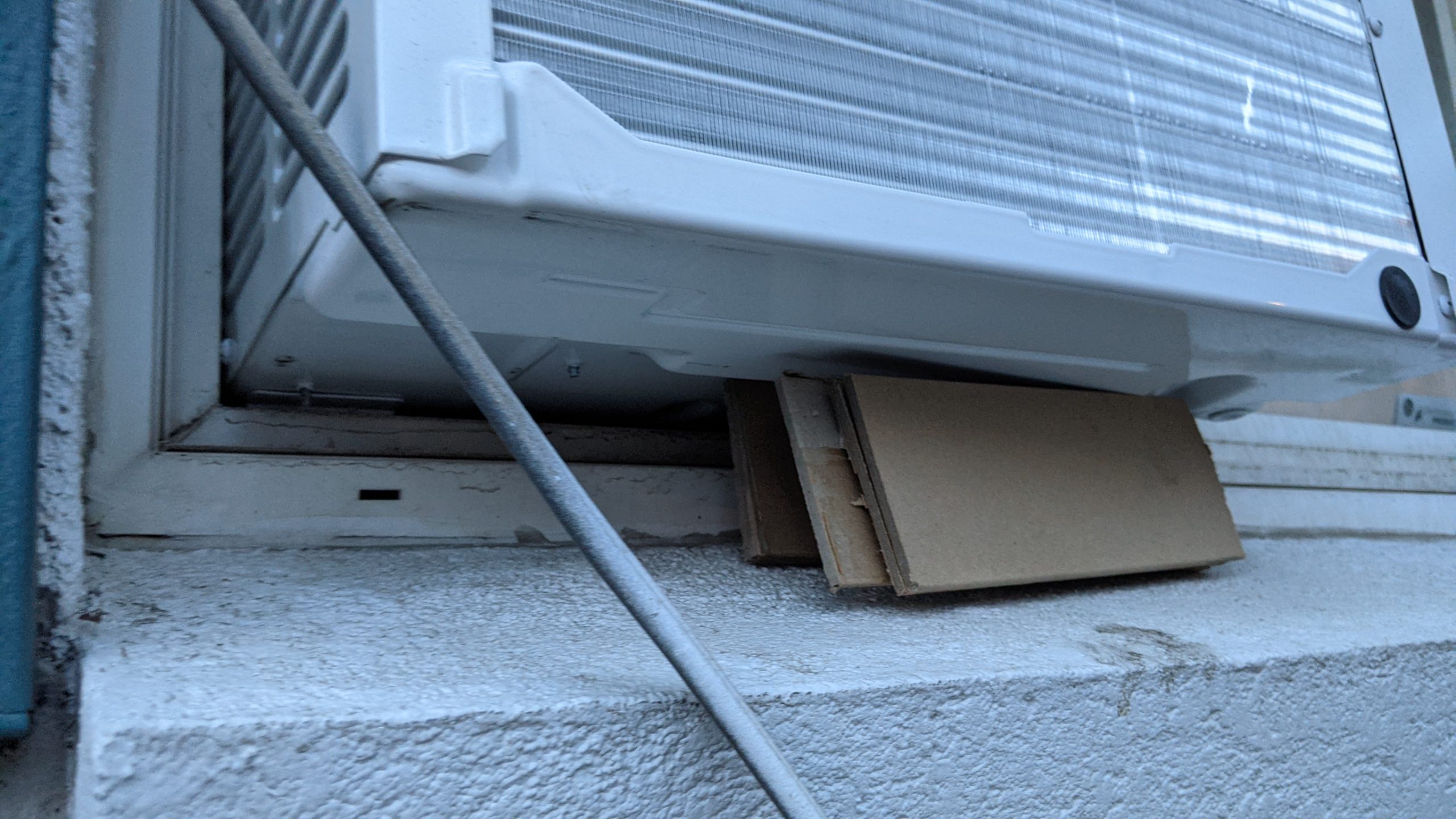 Air conditioning unit precariously placed on a piece of cardboard, depicting poor repair standards